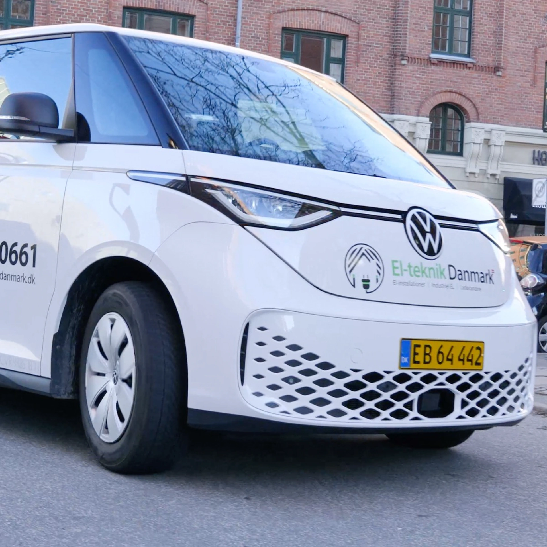 Elbil med logo fra El-teknik Danmark foran en bygning.