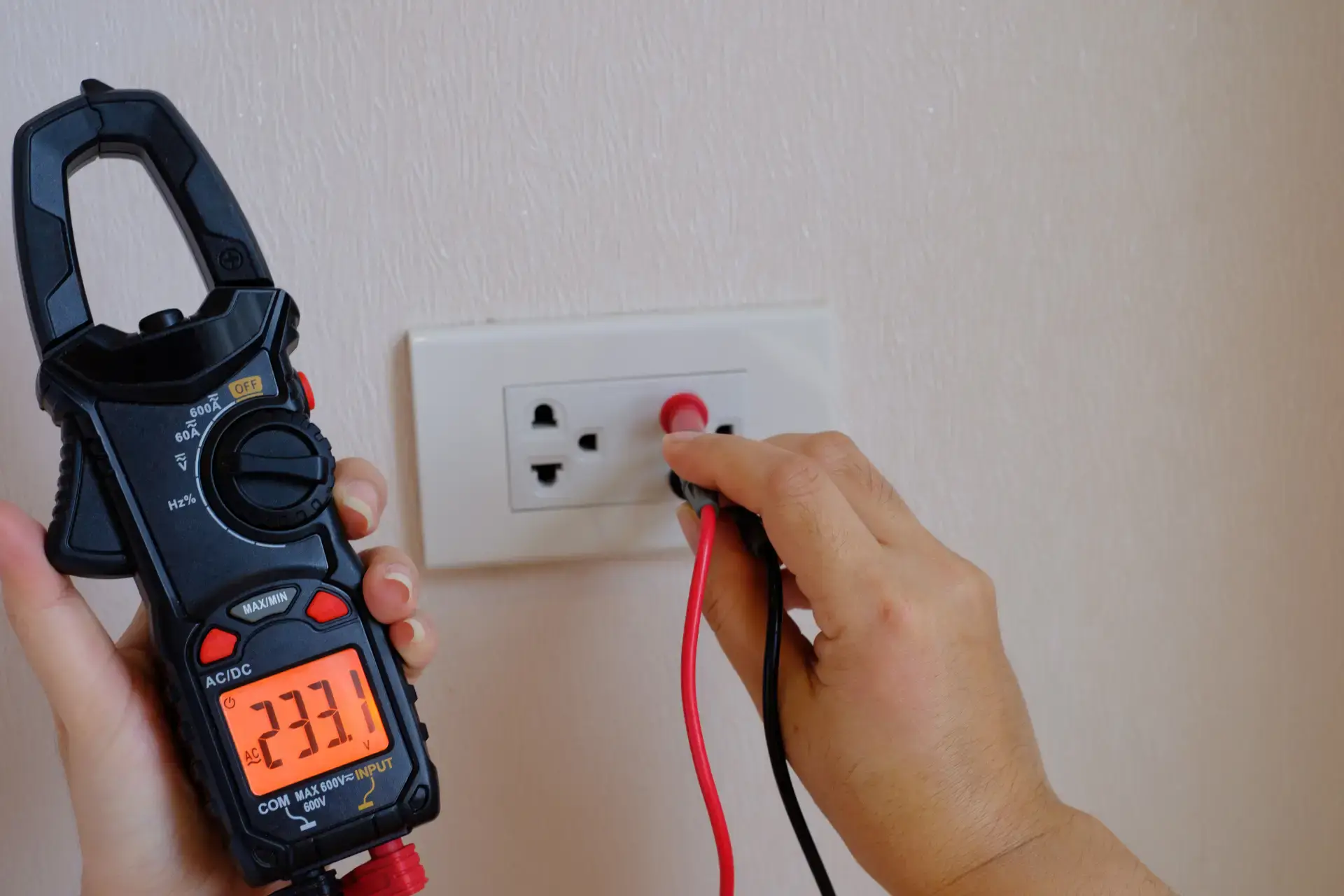 Elektriker måler elektrisk spænding med multimeter i vægkontakt.