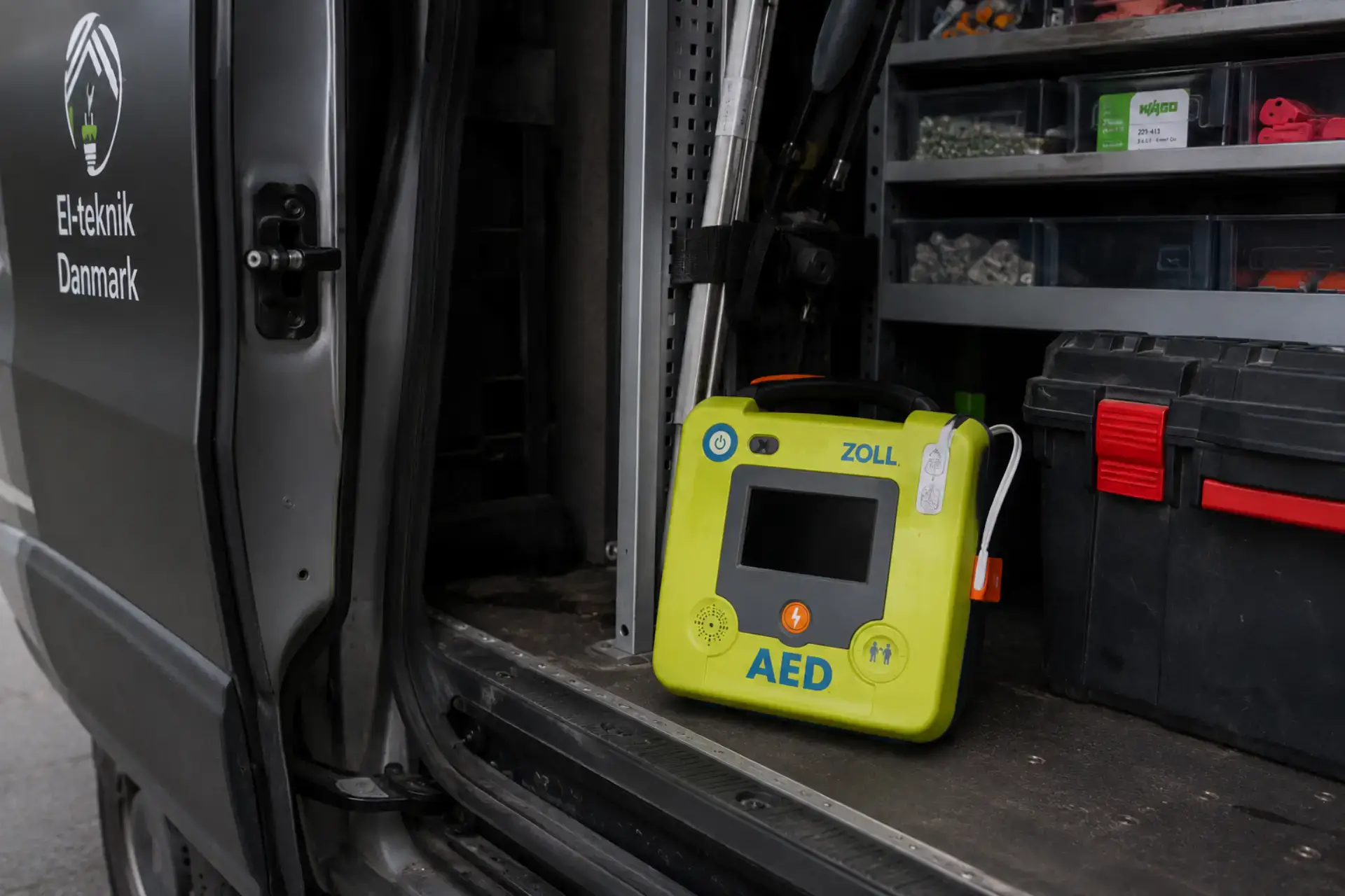 Hjertestarter AED i sort værktøjskasse på værksted.